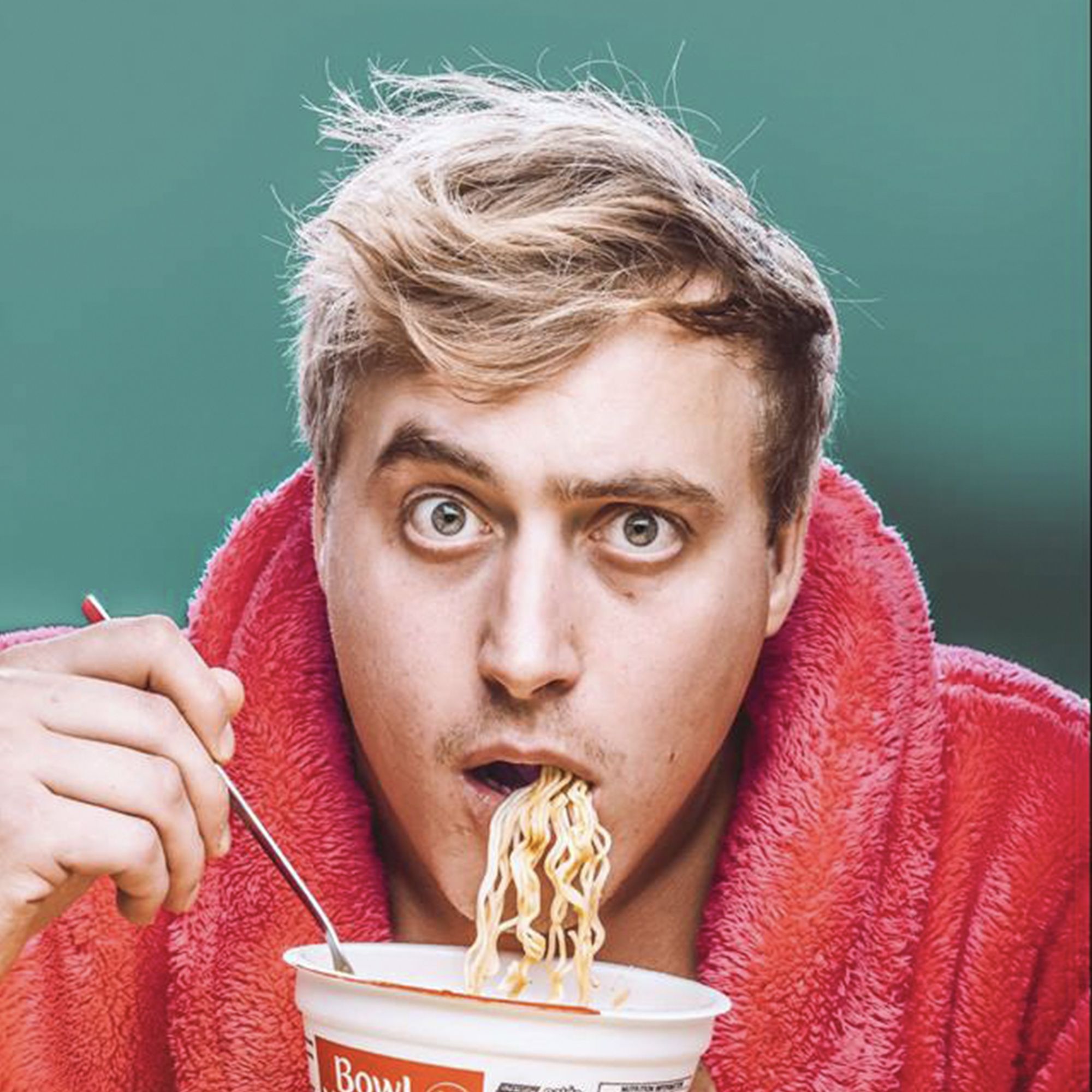 Blue background with man in pink dressing gown eating noodles